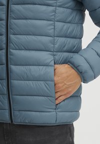 Šviesiai mėlyna, siūtuoto pluošto pūkinė striukė su užtrauktuku priekyje, šonine kišene ir elastingomis rankovėmis. Sklandus paviršius ir elegantiškas dizainas.