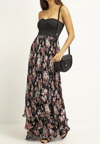 Vestido maxi sin tirantes con un corpiño negro texturizado y una falda negra fluida que presenta un patrón floral en rosa, blanco y acentos dorados.