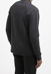 Sudadera negra con cuello redondo, mangas largas y puños acanalados. Textura suave con una silueta ligeramente ajustada.