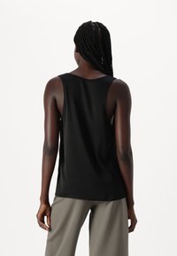 Svart tanktopp laget av et glatt stoff, med en avslappet passform, brede skulderstropper og en avrundet kant. Stylet med grå bukser.