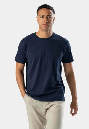 Mørkeblå bomulds t-shirt med rund hals og korte ærmer, båret med lyse beige bukser, glat tekstur og ingen synlige mønstre eller detaljer.