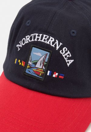 Marine kasket med en rød skygge, der har broderet teksten "Northern Sea" og en farverig sejler-scene med flag.