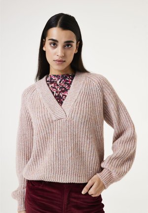 Sweater en tricot texturé rose clair avec un col en V et des poignets côtelés, associé à un blouse à motifs floraux en dessous.