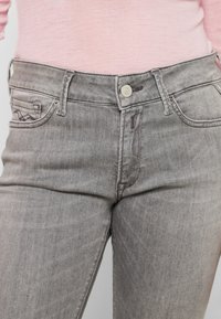 Woman wearing light gray denim jeans and a pink long-sleeve top, showing waist and upper thighs.