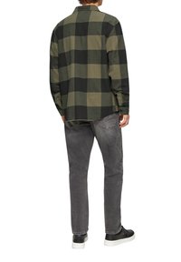 Groen en zwart geblokte flanellen shirt met lange mouwen, gedragen over grijze jeans en zwarte sneakers, gezien van achteren.