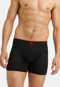 Svarta boxershorts med ett röd elastiskt midjeband som har en logotyp. Tyget verkar mjukt med en slät yta och en åtsittande design.