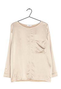 Pitkähiha beige paita, joka on valmistettu sileästä kankaasta. Lantiolla pyöreä kaula-aukko ja yksi rintatasku, jossa on hieno kiilto. Ripustettu mustalle koukulle.