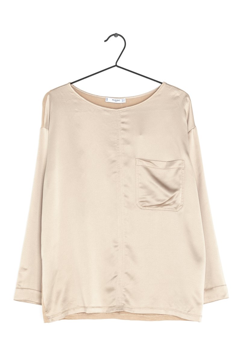 Pitkähiha beige paita, joka on valmistettu sileästä kankaasta. Lantiolla pyöreä kaula-aukko ja yksi rintatasku, jossa on hieno kiilto. Ripustettu mustalle koukulle.