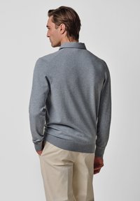 Grauer Strickpullover mit Kragen, langen Ärmeln und geripptem Saum. Glatte Textur, tailliertes Design. Getragen über hellfarbigen Hosen.