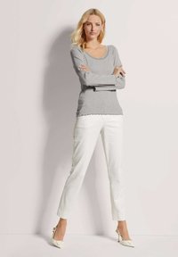 Grijze lange mouwen trui met een geschulpte halslijn, gecombineerd met witte rechte broek en witte hoge hakken. Gladde textuur.