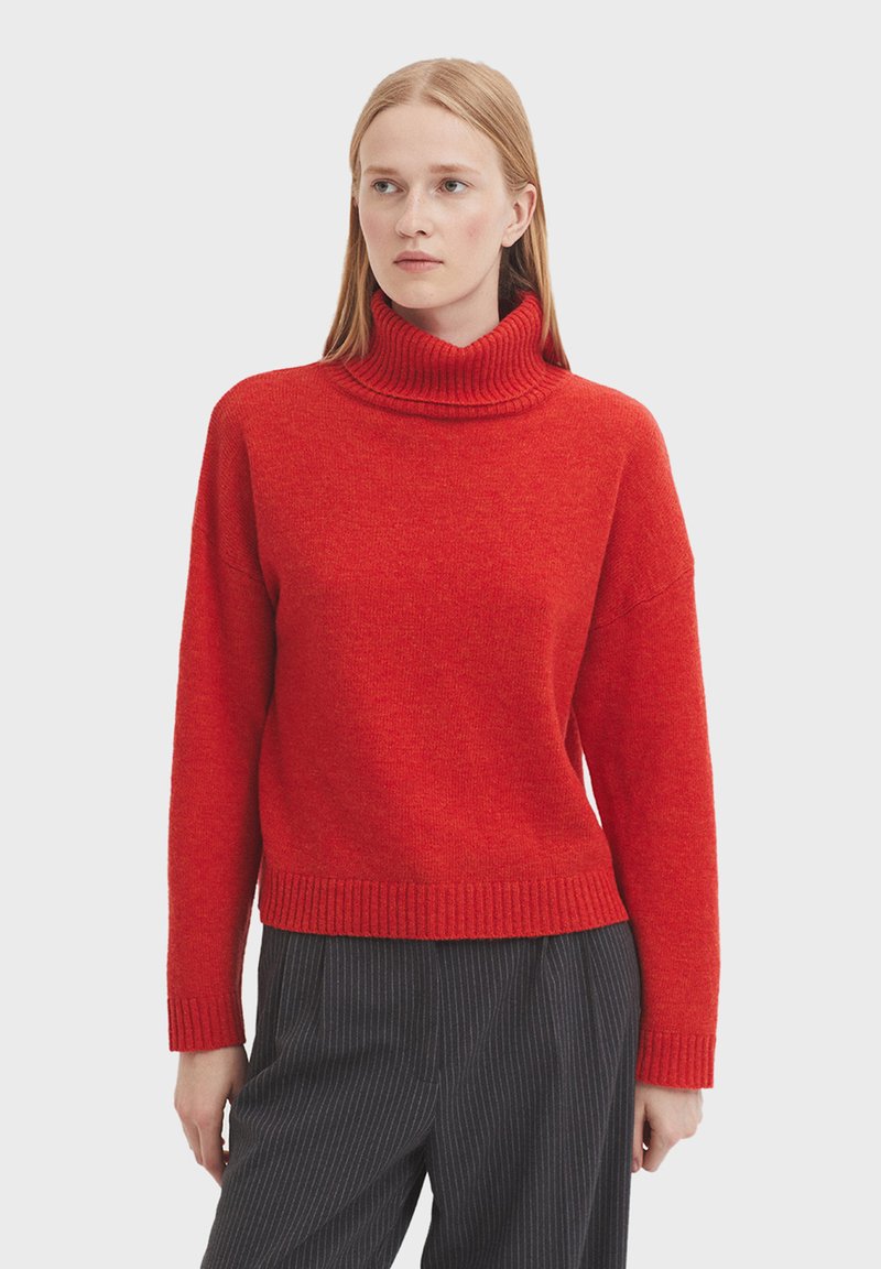 Roten Rollkragenpullover aus Strickstoff mit geripptem Kragen und Saum. Hat einen lässigen Schnitt und überschnittene Schultern. Kombiniert mit gestreiften Hosen.