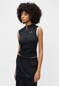 Top deportivo negro sin mangas con cuello alto, cierre con cremallera y acentos blancos en los hombros, combinado con una falda negra con cordón ajustable.