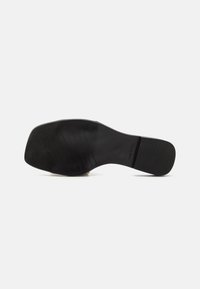 Suola di scarpa in gomma nera con scanalature orizzontali e verticali, dotata di marchio improntato. Design piatto con una base del tallone ampia per stabilità.