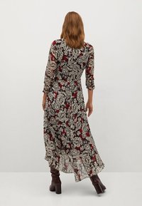 Długa kwiecista sukienka z przezroczystego materiału, zdobiona czarnymi, czerwonymi i beżowymi wzorami, z długimi rękawami i zwiewnym krojem spódnicy. Brązowe kozaki do kolan.