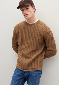 Bruine gebreide trui met geribbelde textuur, ronde halslijn en lange mouwen, gecombineerd met blauwe spijkerbroek.