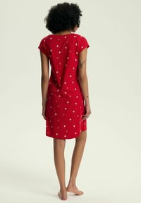 Czerwona sukienka uszyta z miękkiego materiału o luźnym kroju, z złotymi wzorami w diamenty, krótkimi rękawami i długością do kolan.