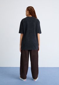 Tricou oversized negru cu mâneci scurte, având o textură estompată. Asortat cu pantaloni lejeri din catifea raiată maro și adidași slip-on.
