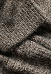 Gros plan sur un tissu tricoté marron doux et duveteux avec une texture côtelée et des fibres visibles formant des couches pliées.