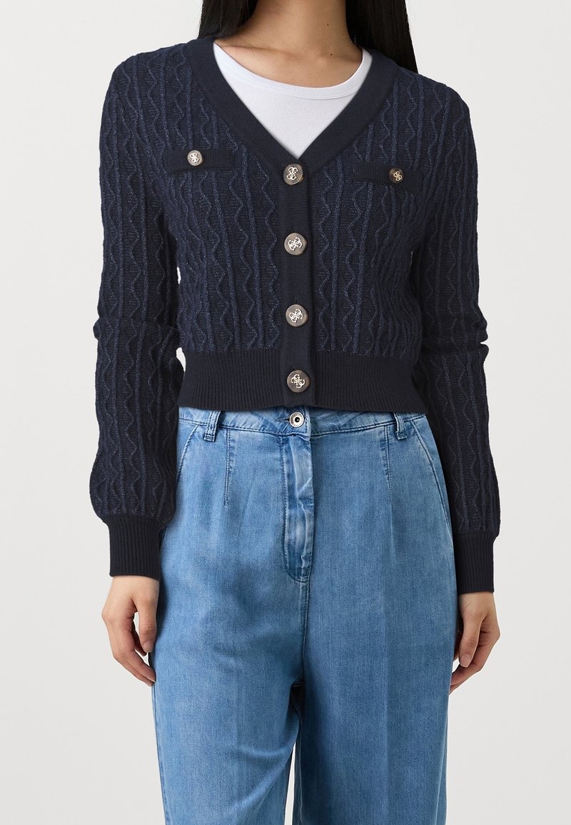 Marineblauer Strickcardigan mit strukturiertem Muster, V-Ausschnitt, langen Ärmeln, aufgesetzten Taschen und Metallknöpfen. Verkürztes Design mit geripptem Saum.