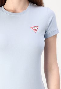 Šviesiai mėlynas prigludęs mar�škinėliai, pagaminti iš minkštos medvilnės, su raudona ir balta trikampio logotipo etikete kairėje krūtinės pusėje. Trumpomis rankovėmis.