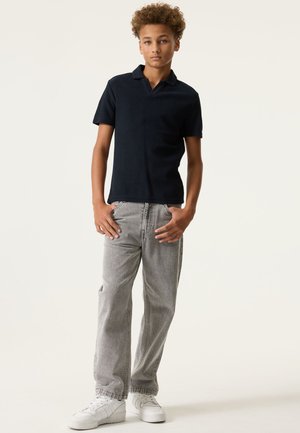 Marineblauw poloshirt met een gestructureerde stof, gecombineerd met lichtgrijze spijkerbroek en witte sneakers. De outfit heeft een klassieke pasvorm en kraag.