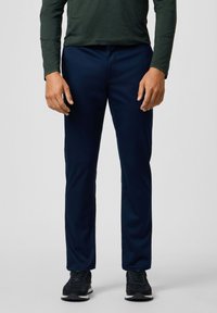 Pantalones ajustados de color azul marino con una textura suave, que cuentan con bolsillos frontales y una cinturilla estándar. Llevados con zapatillas negras.