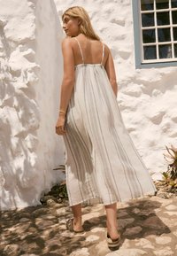 Helles graues Leinenkleid mit dünnen Trägern, das vertikale Streifen aufweist. Durchsichtige Textur, knöchellang, kombiniert mit einfachen Sandalen.