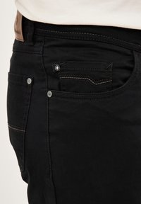 Schwarze Denim-Jeans mit slim fit, dezenten Nähdetails, einer kleinen Vordertasche und metallischen Beschlägen an den Taschen.
