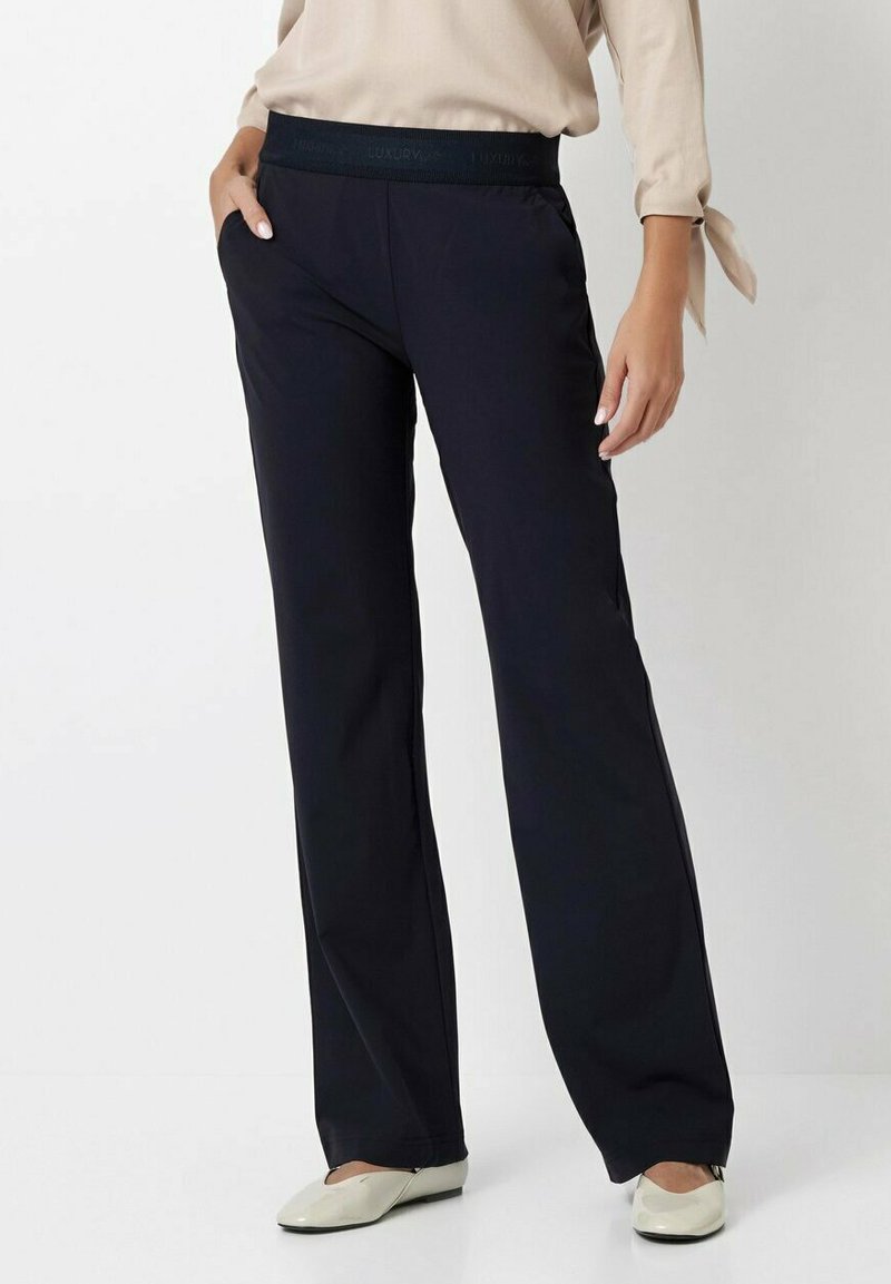 Navy wide-leg pants with a textured elastic waistband, featuring a smooth fabric finish and a modern silhouette, paired with light-colored shoes.