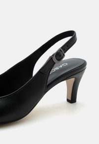 Μαύρο δερμάτινο τακούνι slingback με ρυθμιζόμενο λουράκι με πόρπη και μεσαίο ψηλό καμπυλωτό τακούνι σε λευκό φόντο.