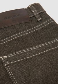 Primer plano del bolsillo trasero de unos vaqueros vaqueros oscuros con costuras blancas y una etiqueta de cuero marrón con la marca REISS.