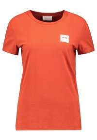 Červené bavlněné tričko s krátkými rukávy a kulatým výstřihem. Má bílou čtvercovou nášivku s nápisem "W.W." na hrudi.