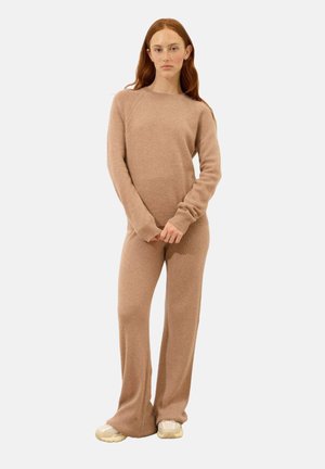 Maglione a coste di un marrone chiaro e pantaloni a campana abbinati, entrambi realizzati in materiale morbido, con maniche lunghe e scollo rotondo classico.