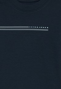 Σκούρο μπλε ύφασμα με λευκές διακεκομμένες οριζόντιες γραμμές και το κείμενο "JACK & JONES" τυπωμένο κοντά στο επάνω κέντρο.