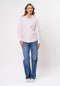 Lichtroze overhemd met verticale strepen, lange mouwen en een klein logo. Gecombineerd met blauwe flared jeans en witte sneakers.