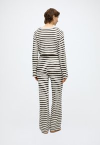 Csíkos kétdarabos otthoni viselet szett krém és fekete színekben, rövidített pulóverrel és bővülő szabású nadrággal, puha, texturált anyagból.