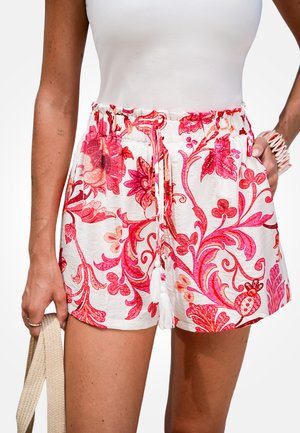 Witte shorts met een roze bloemenpatroon, voorzien van een taille met trekkoord en kwastaccenten. De stof heeft een lichte, gestructureerde uitstraling.
