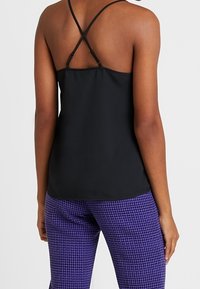 Zwarte mouwloze top met gekruiste schouderbanden, gladde textuur; gecombineerd met paarse houndstooth-patroon broek.