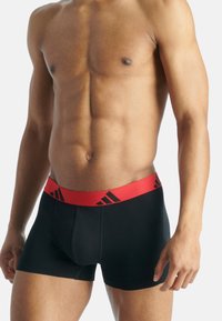 Černé boxerky s červeným pasem, s designem loga, vyrobené z hladkého, elastického materiálu, které těsně obepínají pas.