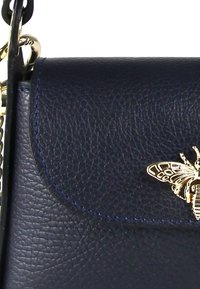 Sac à main en cuir marine avec une finition texturée, doté d'un accent en forme d'abeille en ton doré sur le rabat. Comprend une bandoulière en chaîne métallique.