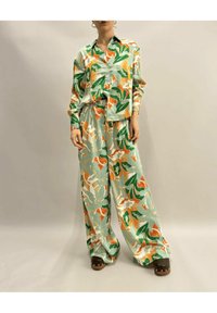 Camicia di seta leggera azzurro con motivo floreale e pantaloni a gamba larga con accenti verdi, arancioni e bianchi, dotati di bottoni e dettaglio in vita legato.