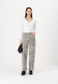 Cárdigan corto de manga larga blanco con textura de canalé y cierre de botones, combinado con pantalones de pierna ancha de patrón cebra en gris y zapatos de plataforma negros.