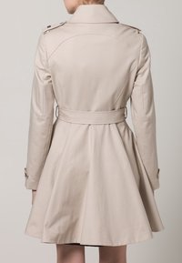Beżowy płaszcz trench z rozkloszowanym kształtem, z ozdobnymi shoulder epauletami i zawiązywanym paskiem w talii; wykonany z gładkiego, lekkiego materiału.