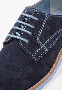 Scarpa in suede blu navy con cuciture azzurro chiaro, sei fori per i lacci, punta arrotondata e suola in contrasto azzurro chiaro.