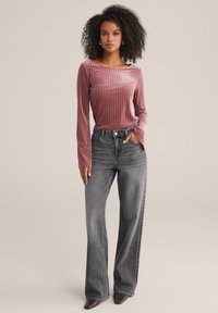 Pika, lõhikuga, roosa särk, millel on paadikaelus, koos kõrge vöökoha ja laia jalgadega hallide teksadega, millel on nööbiga sulgur ja kerge tuhm tekstuur.