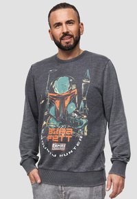 Sudadera gris de mezcla de algodón, con un gráfico colorido de Boba Fett, puños acanalados y un cuello redondeado. El texto incluye "Caza recompensas."