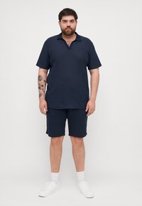 Tengerés csíkos, V nyakú, rövid ujjú póló, hozzá illő rövidnadrággal párosítva. A modellen fehér edzőcipő és crew zokni van.