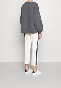 Sudadera gris de gran tamaño con hombros caídos, combinada con pantalones recortados blancos que presentan franjas laterales en azul marino, terminando con zapatillas blancas.
