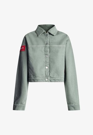 Chaqueta vaquera corta de color verde claro con mangas largas, cierre de botones, cuello y parche rojo en la parte superior izquierda de la manga.