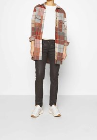 Chemise en flanelle à carreaux dans des tons rouille, rose et gris. Manches longues, boutonnage devant, deux poches poitrine, associée à un jean noir et des baskets blanches.